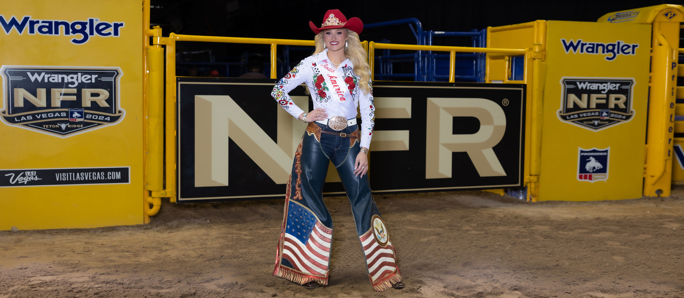 Miss Rodeo America, Callie Mueller, wearing a white button-down shirt, red hat, and chaps, posing in the arena at the National Finals Rodeo.